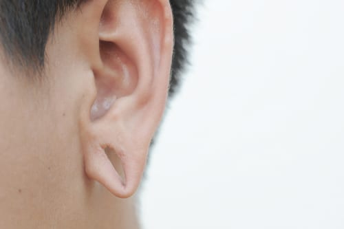 A man 's ear with the tip of his thumb up.