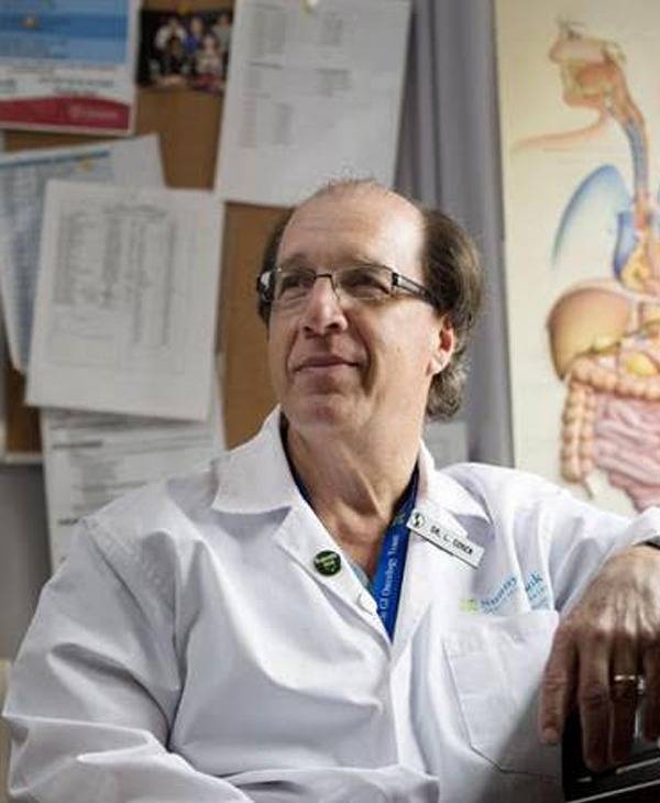 A man in white lab coat sitting next to a wall.