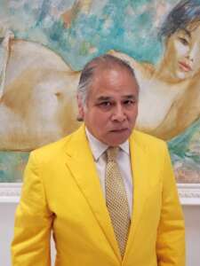A man in a yellow suit standing next to a painting.