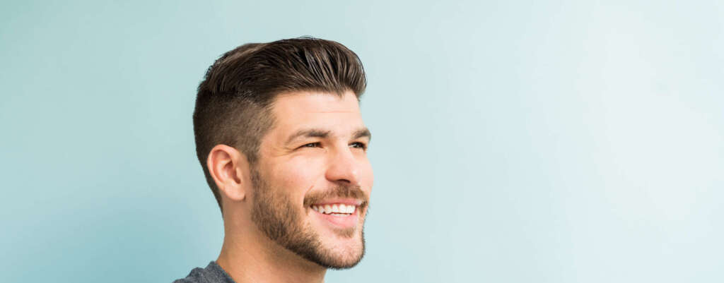 Closeup of smiling young man looking away while standing against turquoise background