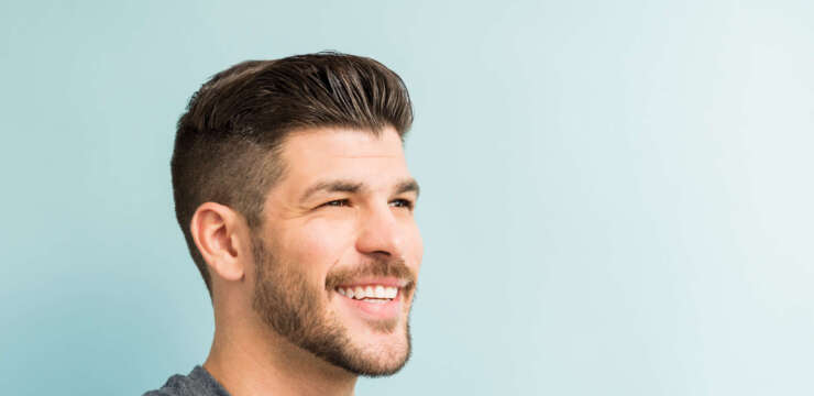 Closeup of smiling young man looking away while standing against turquoise background